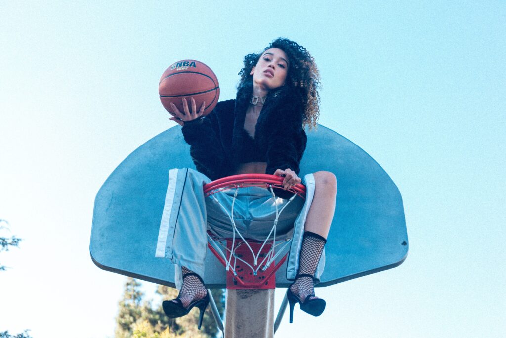Girl sitting on basketball goal holding ball.